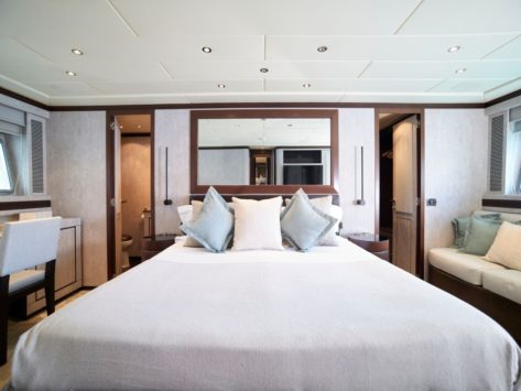 Gran suite principal del yate Mangusta 92 con baño privado, vestidor, sofá y escritorio.
